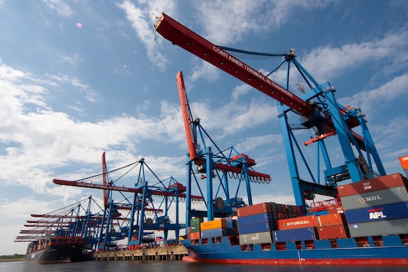 two ships with cargo docked at port with several container cranes above