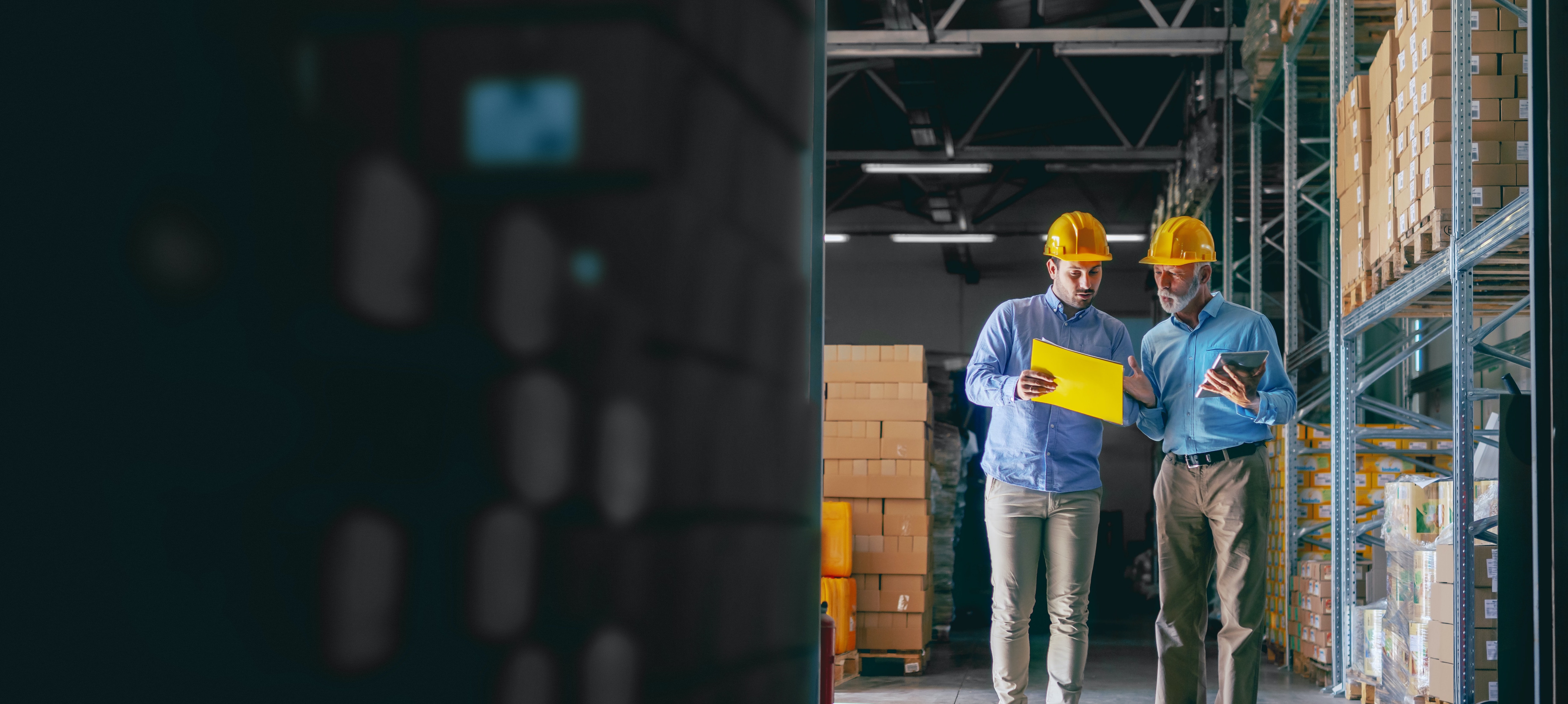Two men reviewing some documentation next to a warehouse shelf